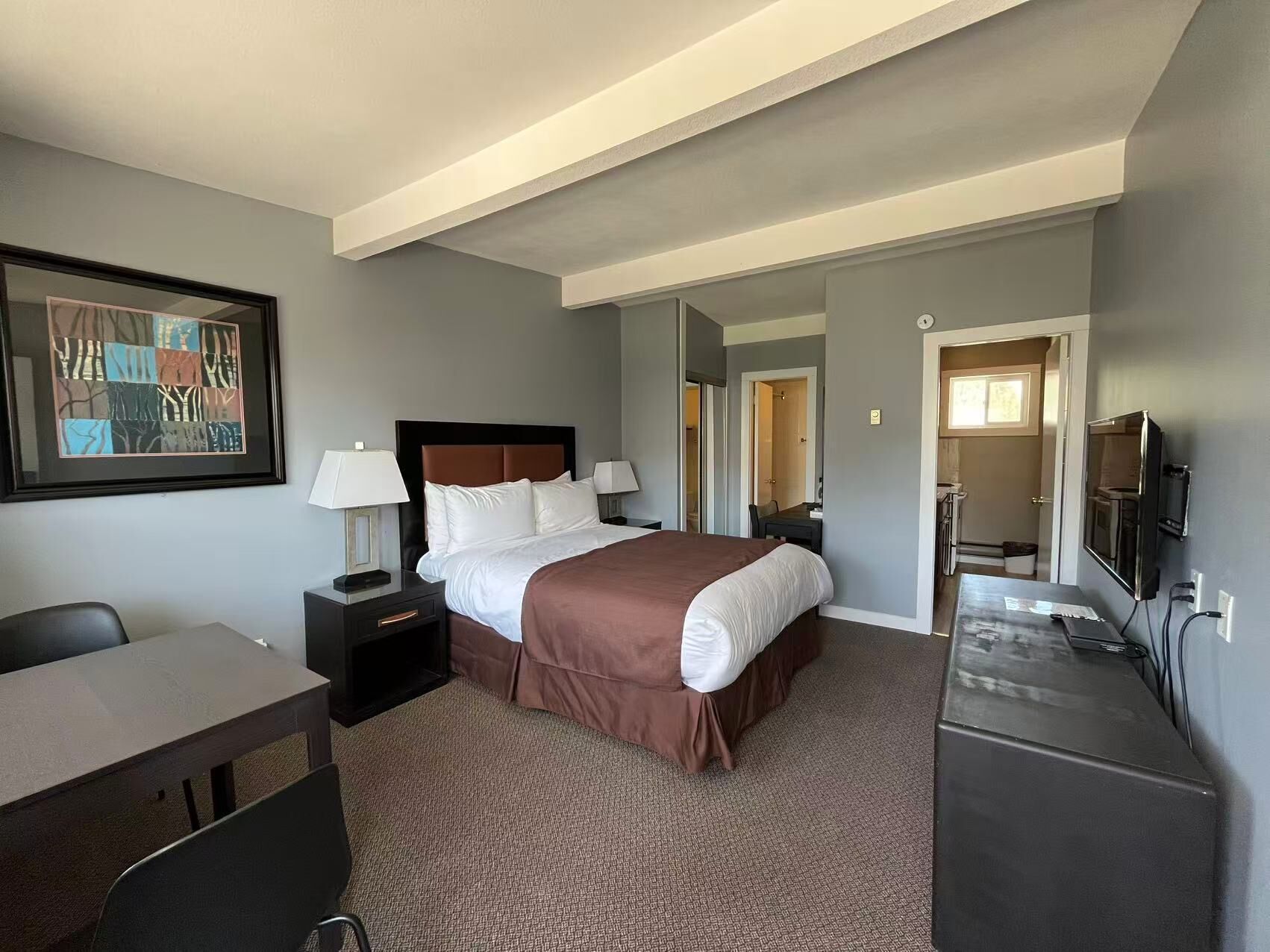 A hotel room with a bed, bedside tables, a desk, a chair, a TV, and a mirror.