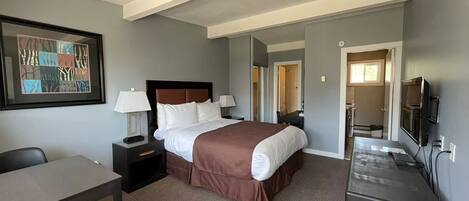 A hotel room with a bed, bedside tables, a desk, a chair, a TV, and a mirror.