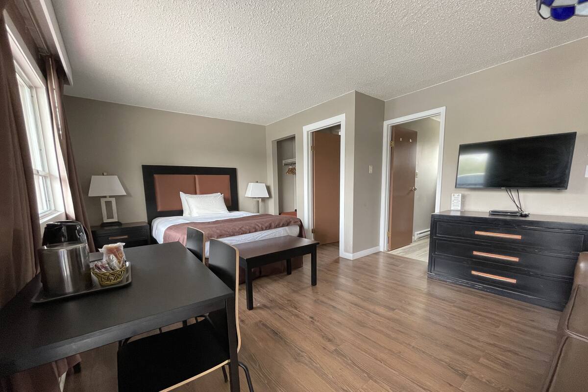 Una habitación de hotel con cama, mesitas de noche, un escritorio con silla, cómoda, televisor y ventana con cortinas.