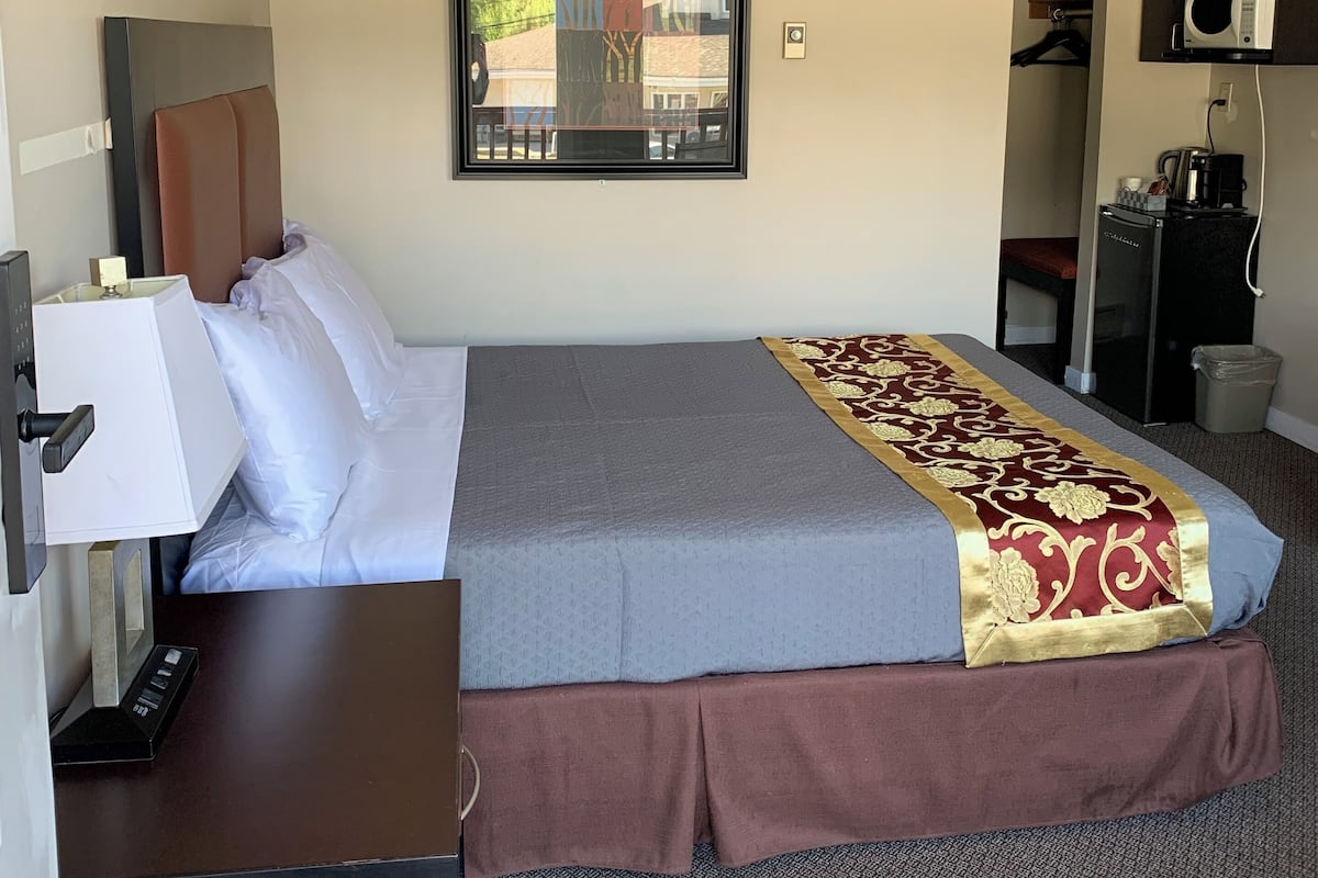 Habitación de hotel con cama, escritorio con lámpara, microondas y cafetera.