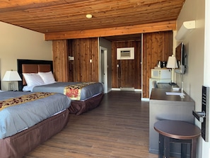 Une chambre d’hôtel avec deux lits, un bureau avec une chaise, une télévision et une kitchenette.