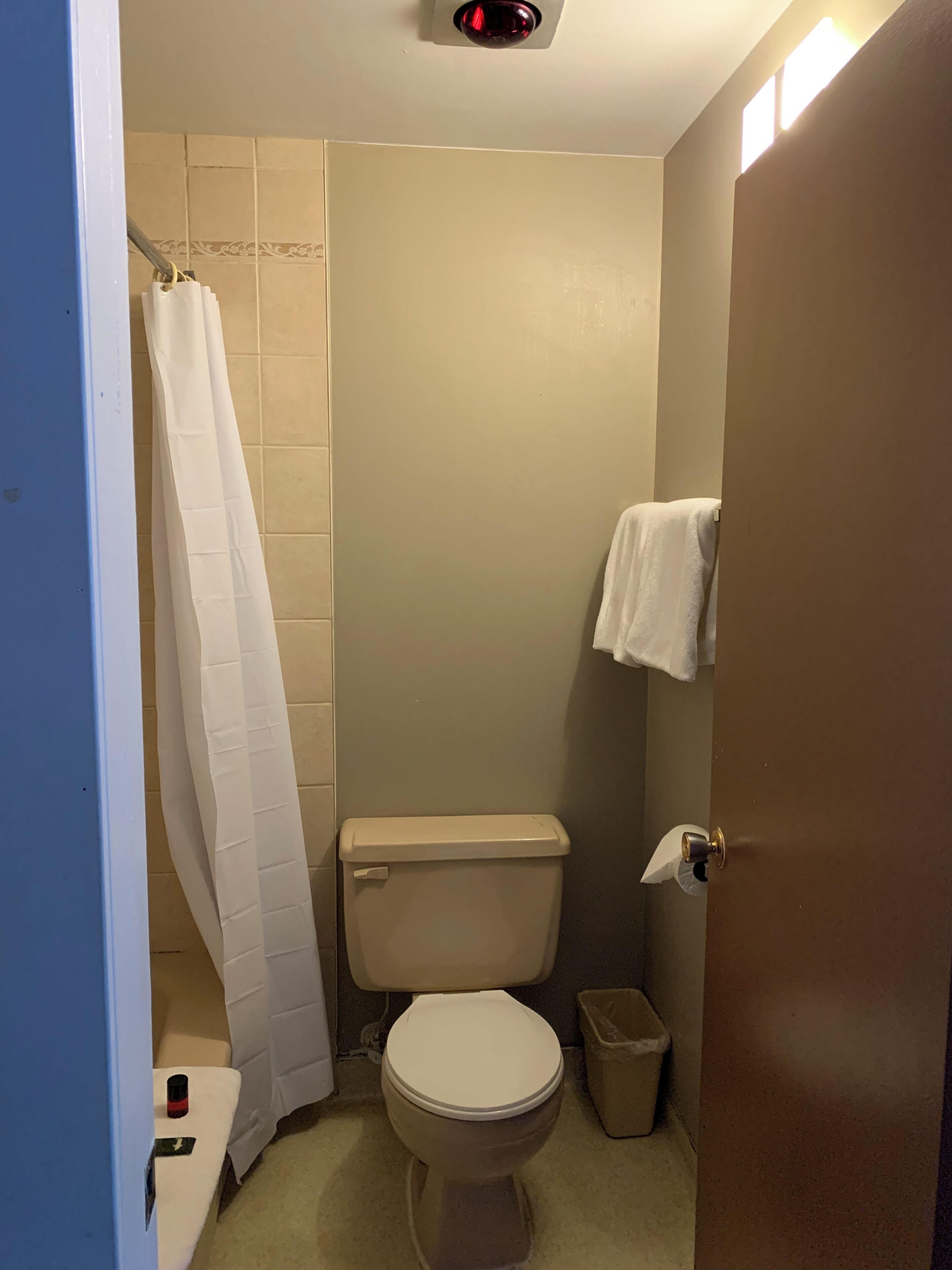 A small bathroom with a toilet, a shower curtain, a towel rack, and a trash bin.