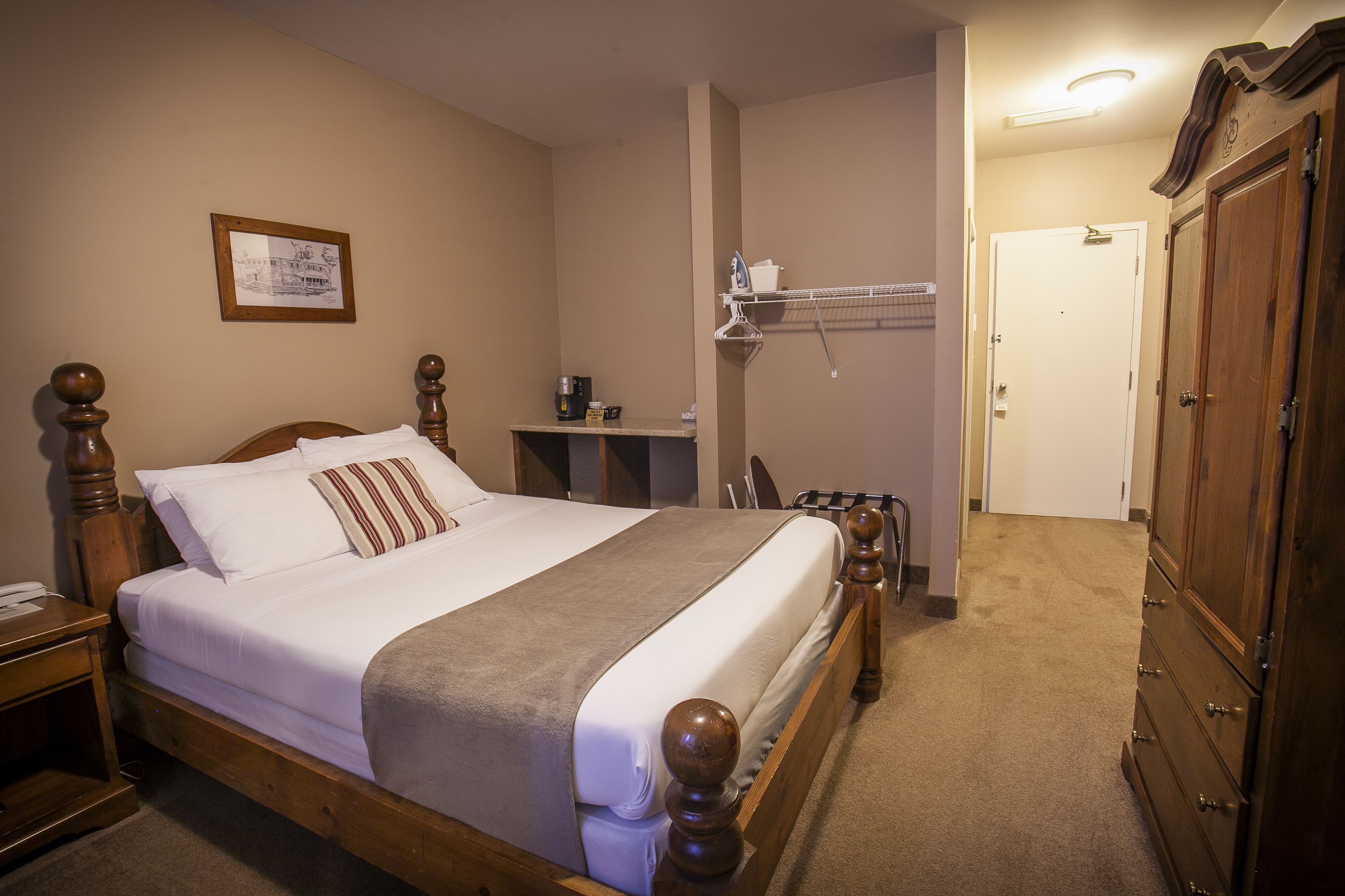 A neatly made bed with a wooden headboard, a bedside table with a lamp, and a wall-mounted shelf with a kettle and cups.