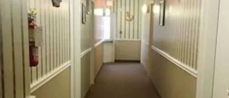 A narrow, carpeted hallway with white walls and vertical stripes, leading to a door at the end.