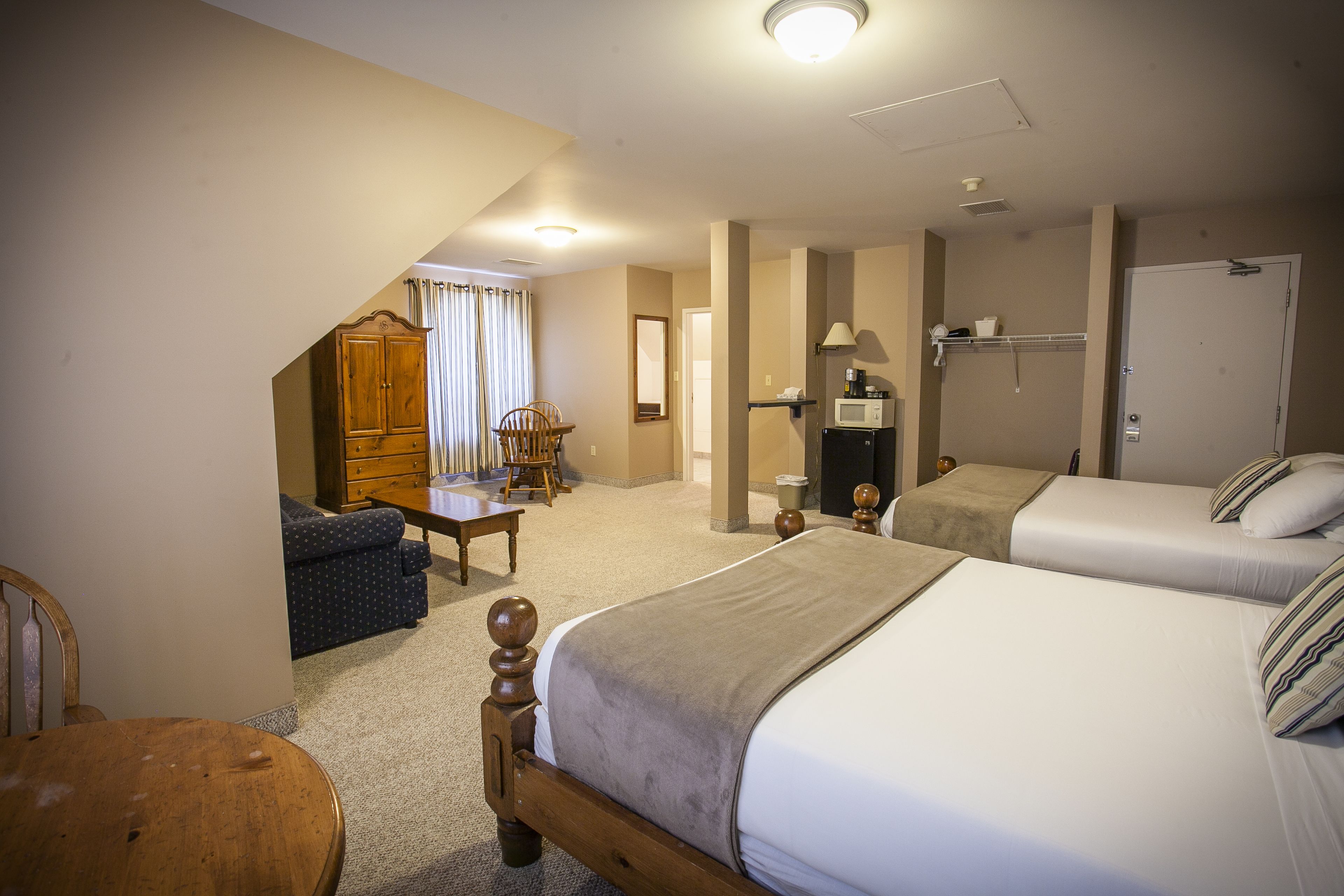 A hotel room with two beds, a wooden wardrobe, a desk, and a chair.