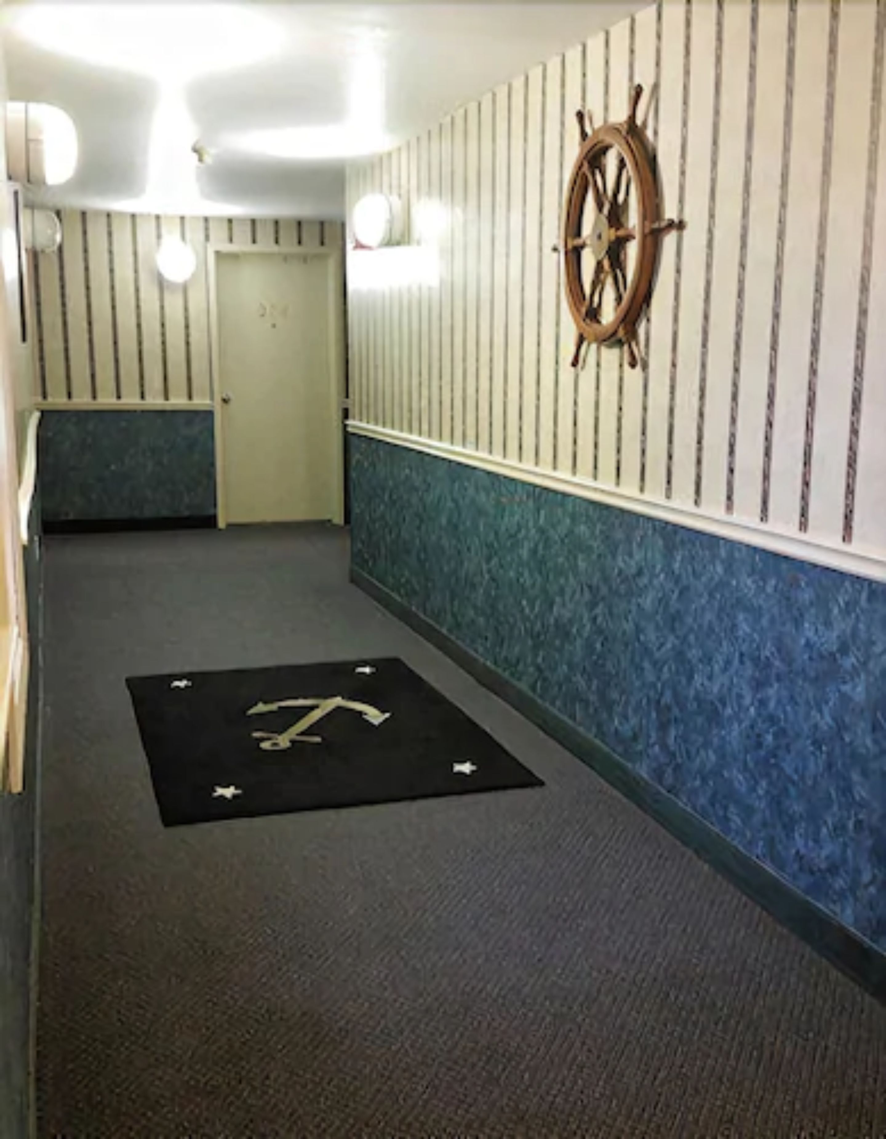 Un corridoio con decorazioni a tema nautico, un tappeto nero con frecce direzionali e una porta in fondo.