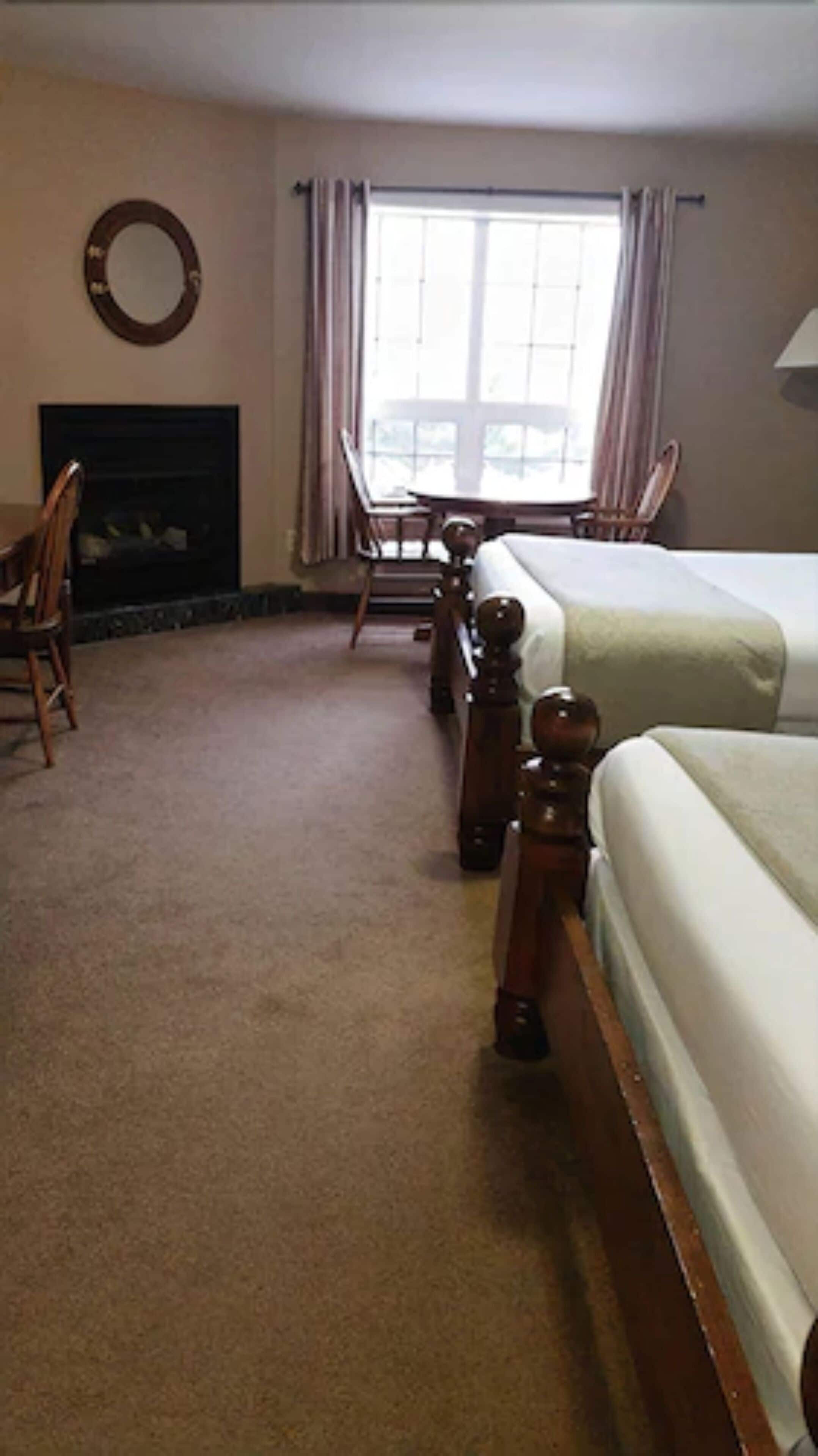 A hotel room with a large window, a fireplace, two beds, and a dining table.