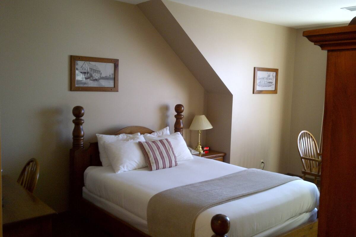 Un lit bien fait, avec une tête de lit en bois, une lampe de chevet et deux tableaux encadrés accrochés au mur.
