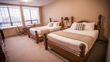 Quarto de hotel com duas camas de madeira, uma mesinha e uma cadeira.