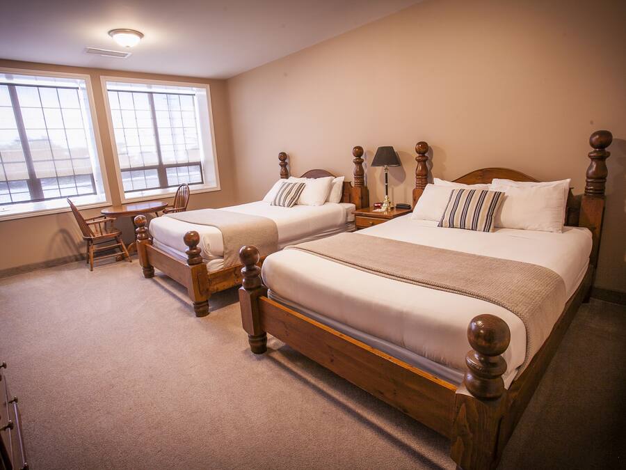 Quarto de hotel com duas camas de madeira, uma mesinha e uma cadeira.