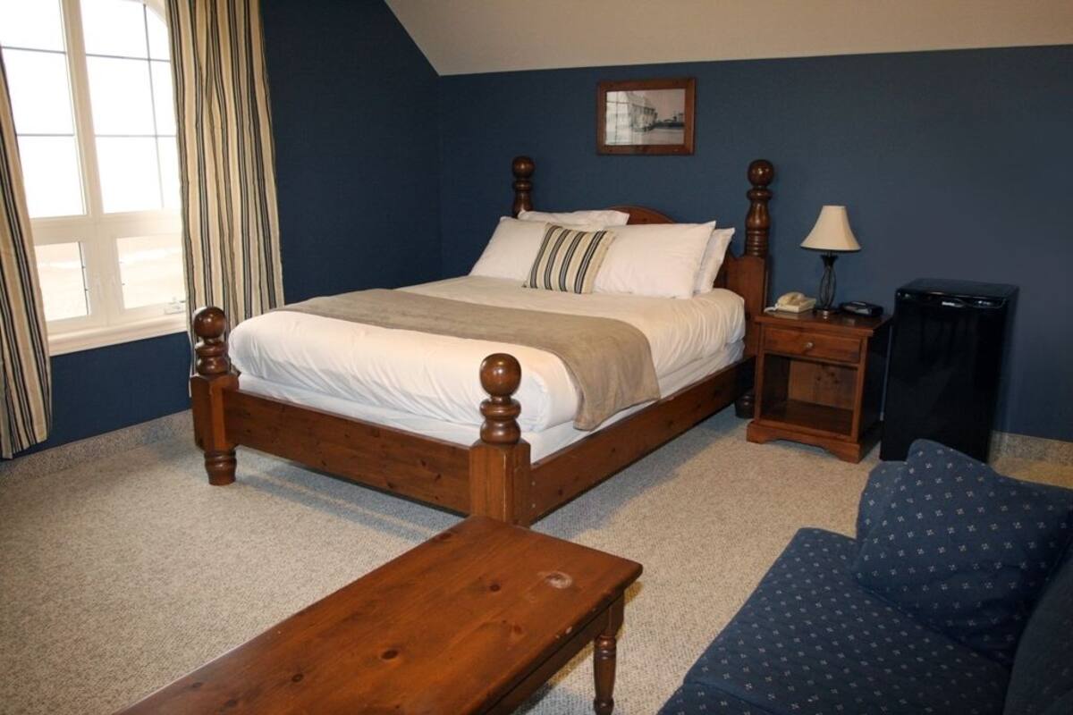 Une chambre à coucher avec un lit en bois, une table de chevet, une lampe, une chaise et une fenêtre avec des rideaux.