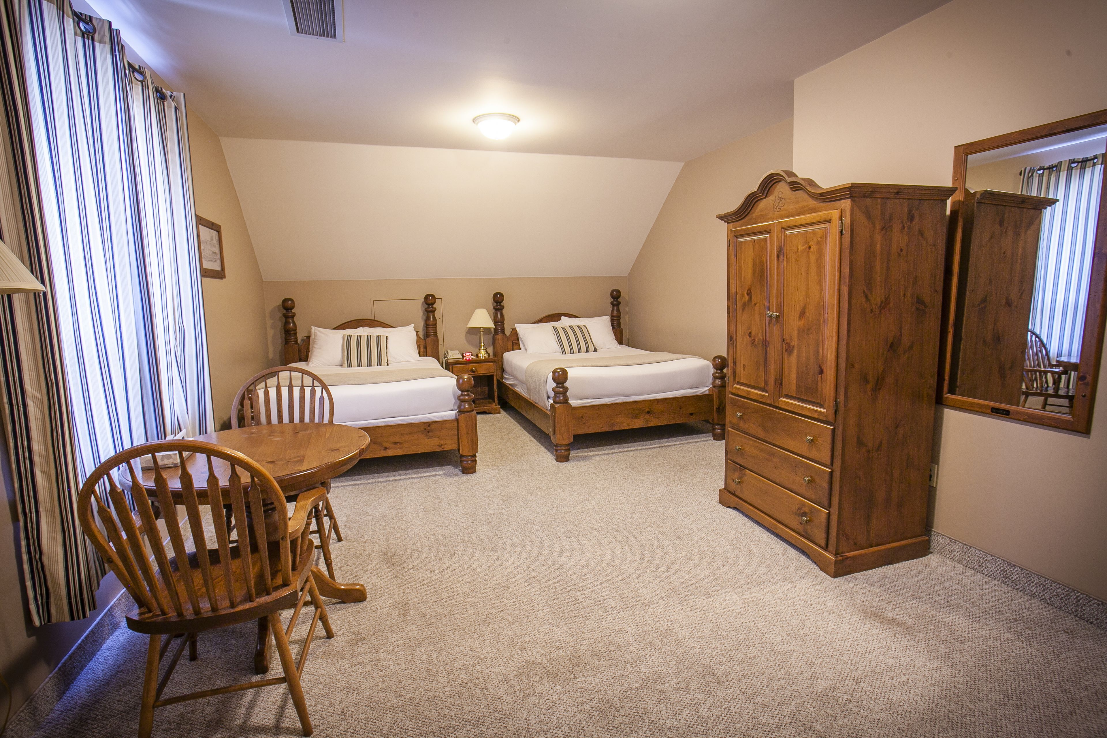 Un dormitorio con dos camas de madera, un armario de madera, una mesa de comedor de madera con sillas y una ventana con cortinas.