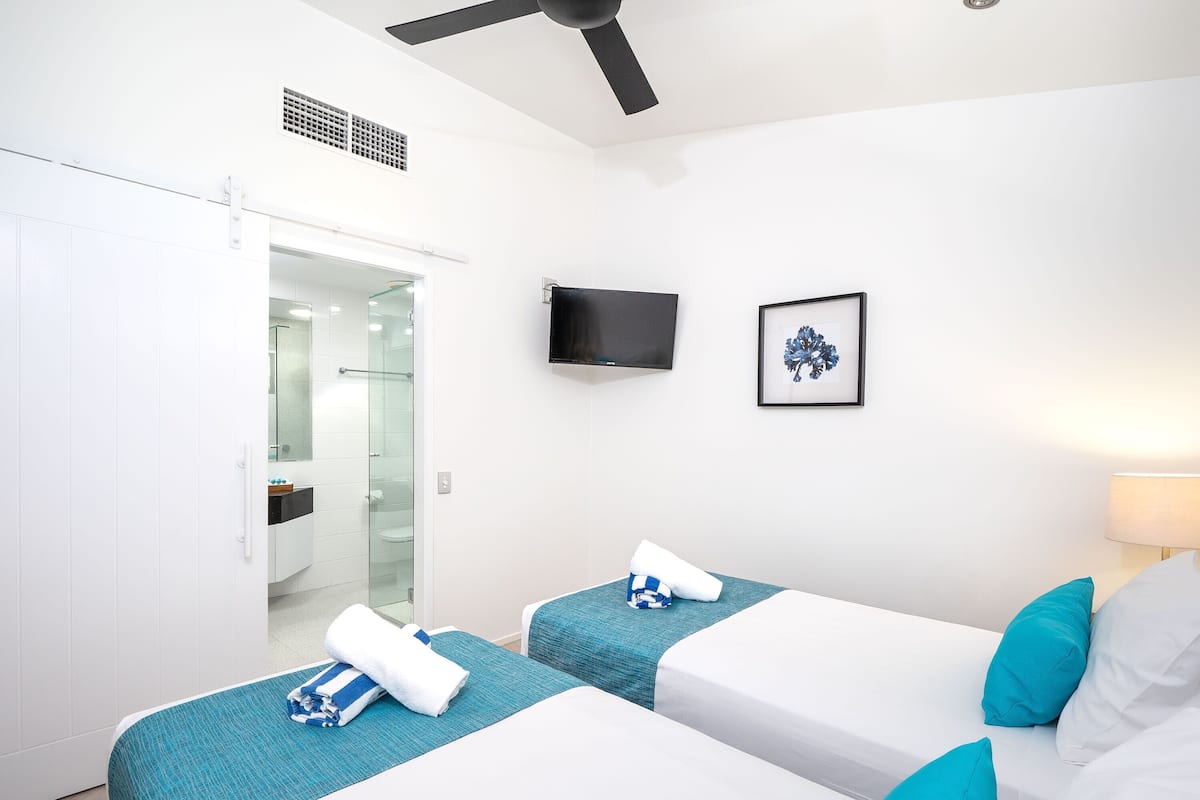 Ein Hotelzimmer mit zwei Betten, einem Fernseher, einem gerahmten Bild und einem Deckenventilator.