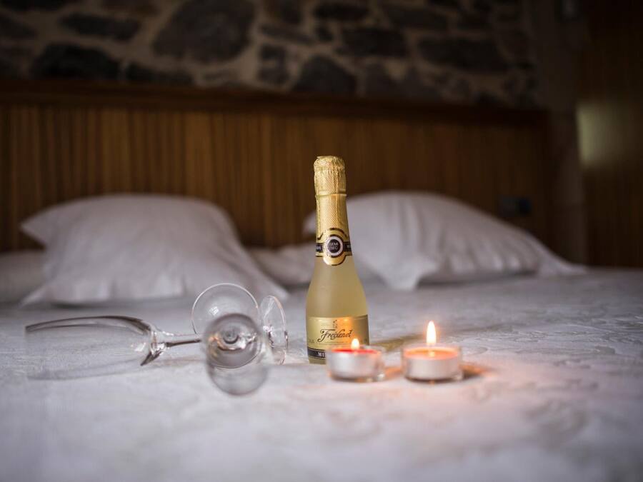 Una cama con una botella de champán, dos copas y una vela encendida.