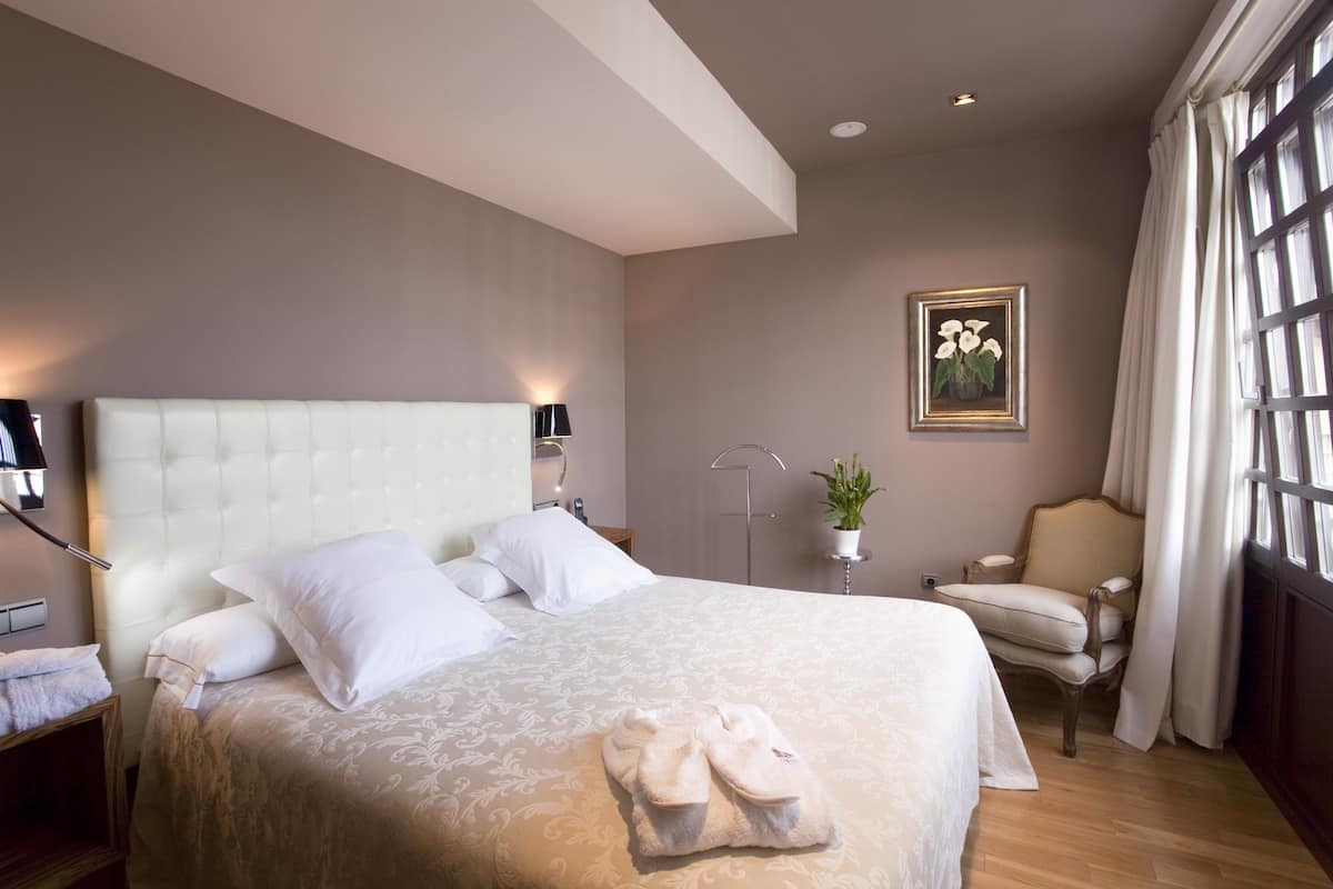 Une chambre d’hôtel avec un grand lit, une chaise, une plante en pot et un tableau au mur.
