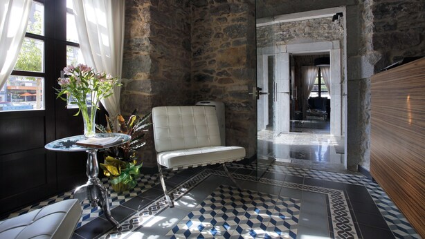 Una habitación con pared de piedra, un banco blanco, una mesita con un jarrón y un suelo estampado.