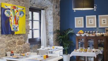 Uma sala de jantar com paredes de pedra, um quadro de vaca colorido e um buffet com diversos alimentos.