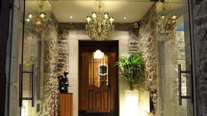 Un pasillo de paredes de piedra con una puerta de madera, un candelabro y una planta en maceta.