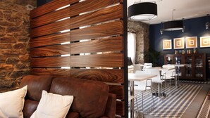 Un interior moderno con una pared de piedra, un separador de listones de madera, un sofá de cuero marrón, taburetes de bar blancos y un suelo con diseño.