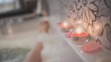A bathtub with a candle, pink bath bomb, and a wall with a floral design.