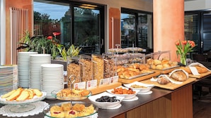 A buffet with various food items, including pastries, fruits, and sandwiches, arranged on a wooden table with a view of the outdoors through large windows. - Geranio au Lac (Muralto)