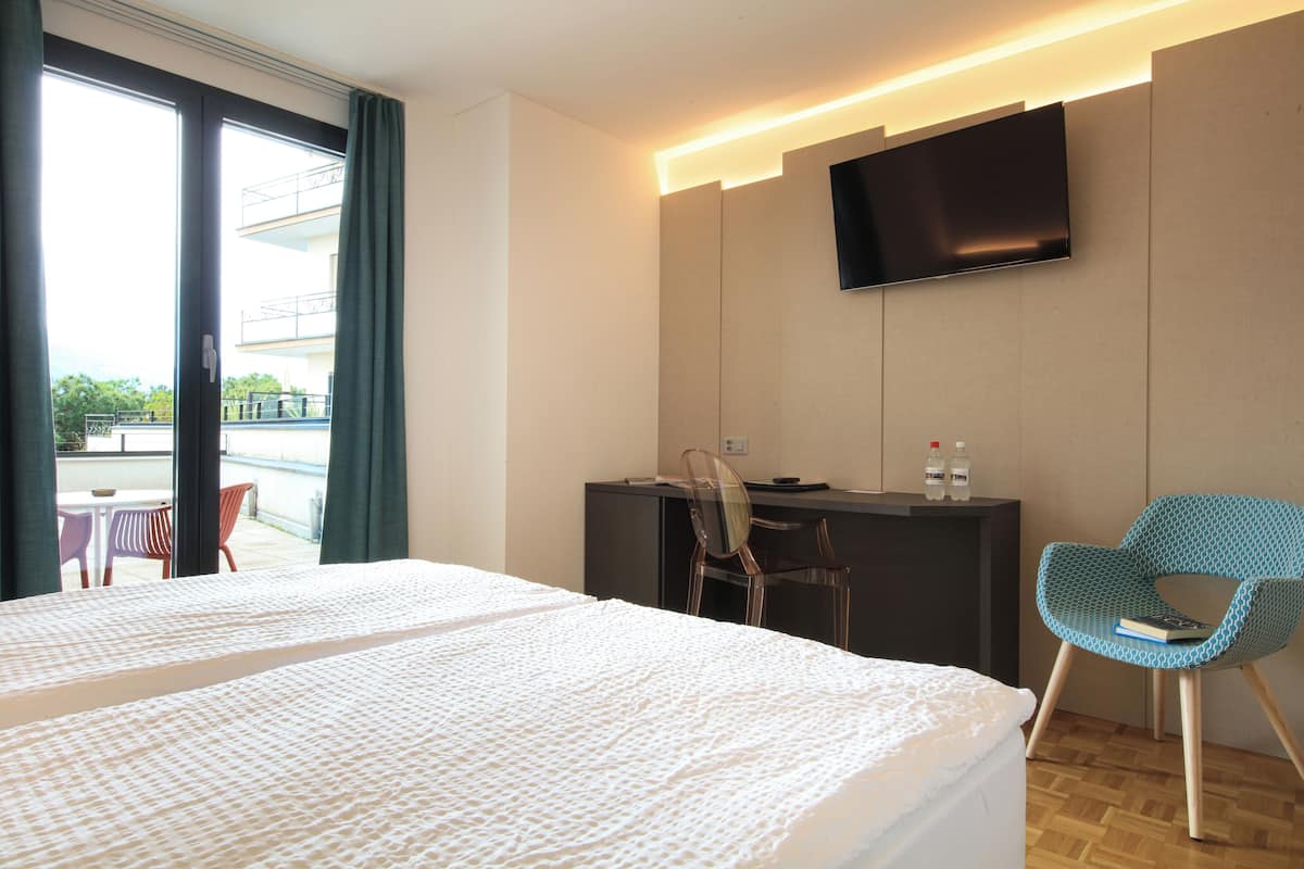 Ein Hotelzimmer mit Bett, Schreibtisch, Stuhl, Fernseher und Blick ins Freie.