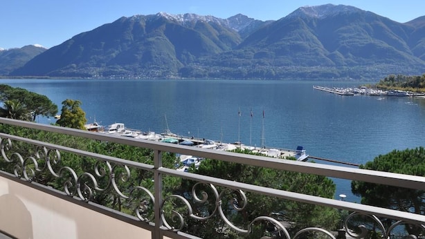 A balcony with a view of a lake, mountains, and a marina with boats. - Geranio au Lac (Muralto)