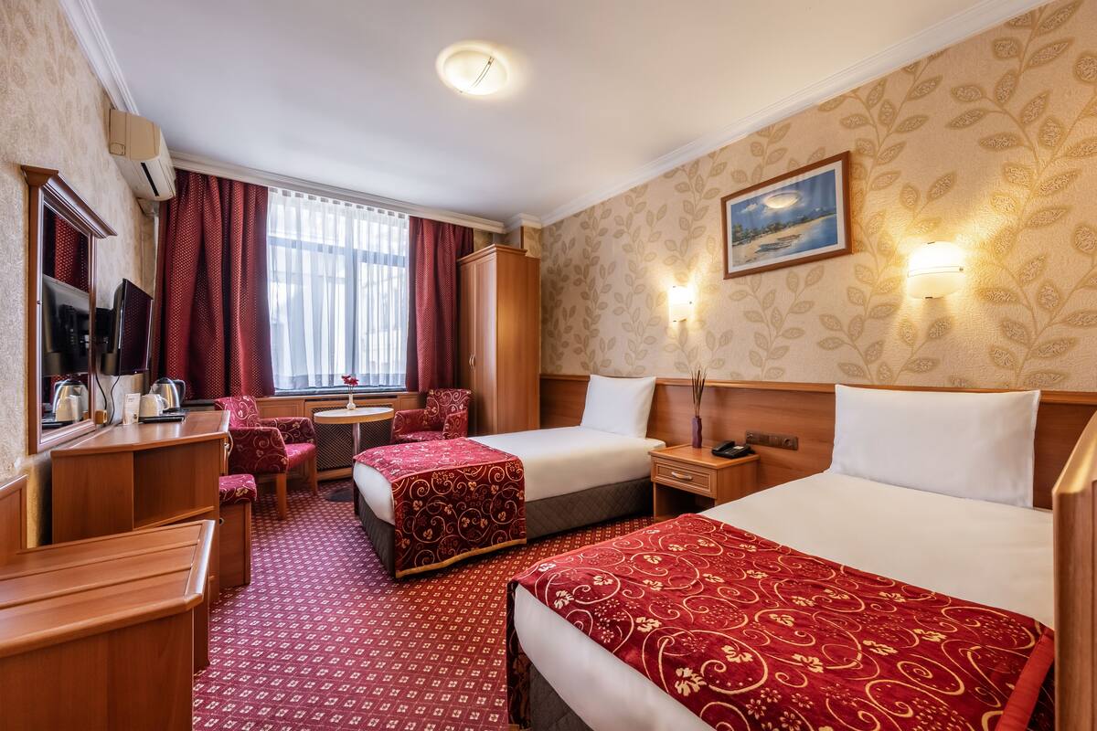 A hotel room with two beds, a desk, a chair, a TV, and a window with curtains.