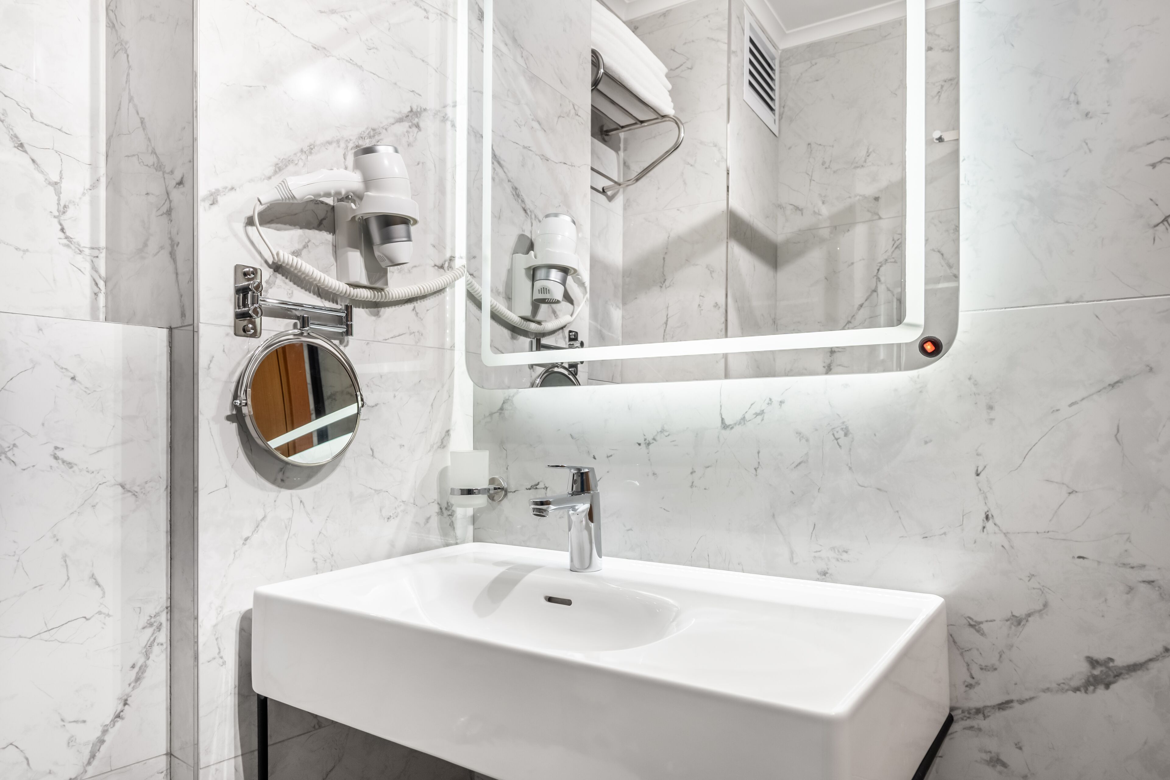 Une salle de bain moderne avec un lavabo blanc, un miroir rond et un sèche-cheveux fixé au mur.