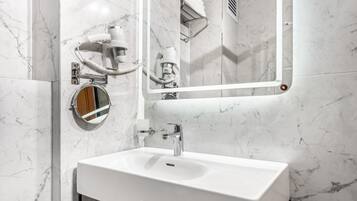 Une salle de bain moderne avec un lavabo blanc, un miroir rond et un sèche-cheveux fixé au mur.