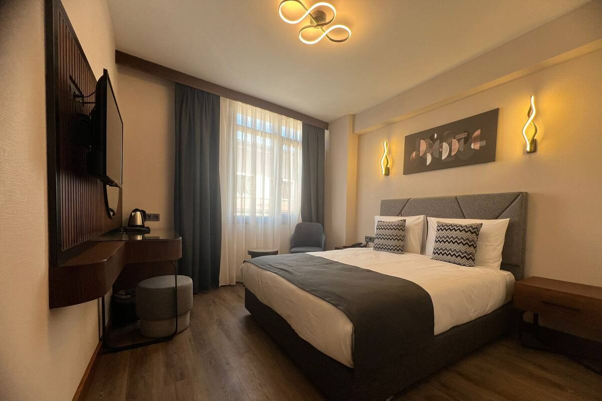 A modern hotel room with a large bed, a desk, and a chair.