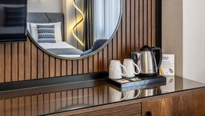 Une chambre d’hôtel avec un mur lambrissé en bois, un grand miroir, un lit avec une tête de lit grise et une machine à café sur la table de chevet.