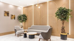 Un hall d’entrée moderne avec un canapé gris, deux fauteuils, une table basse ronde et deux plantes en pot.