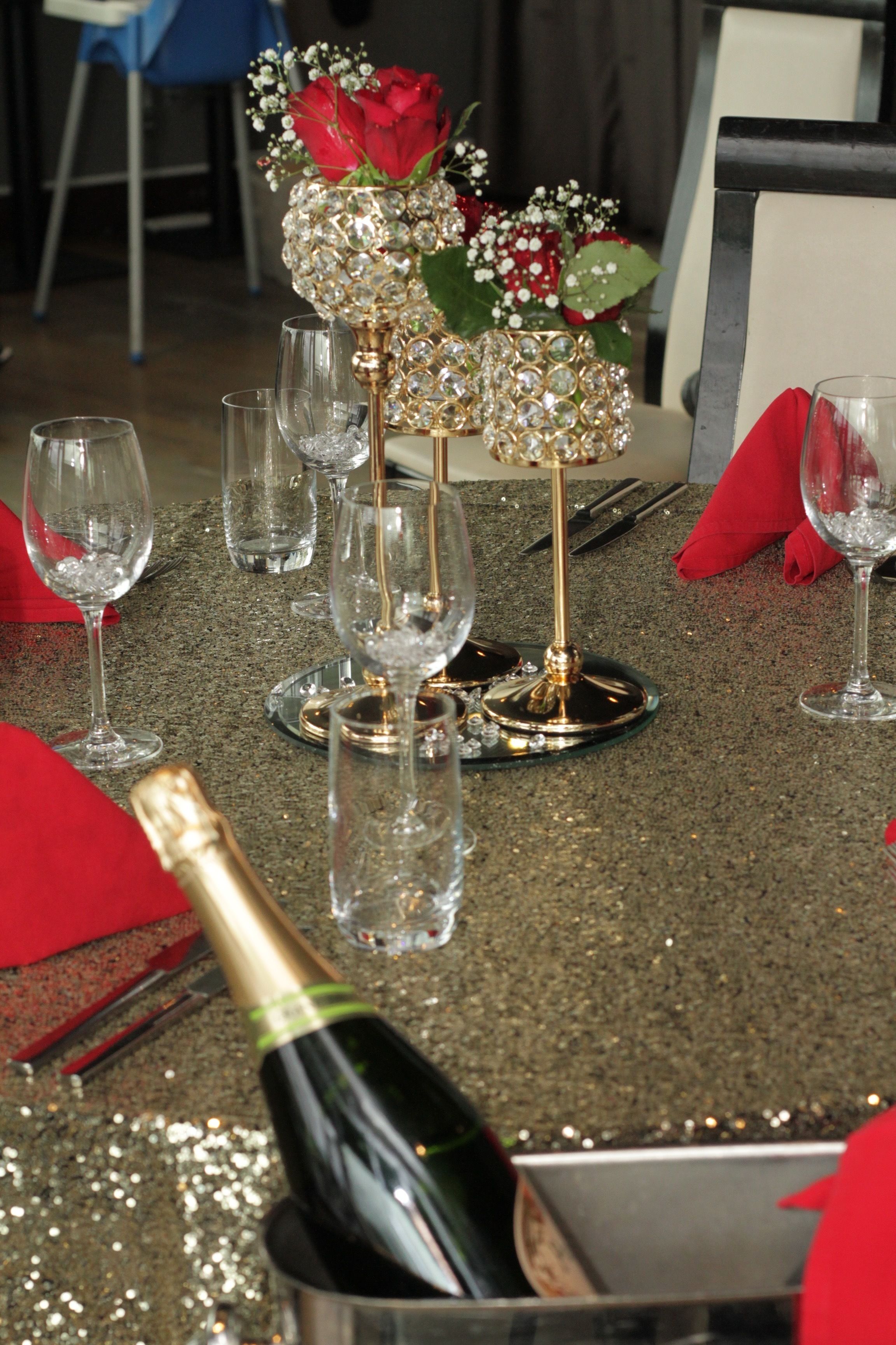 A table set with wine glasses, a champagne bottle, and a decorative centerpiece with flowers and crystals.