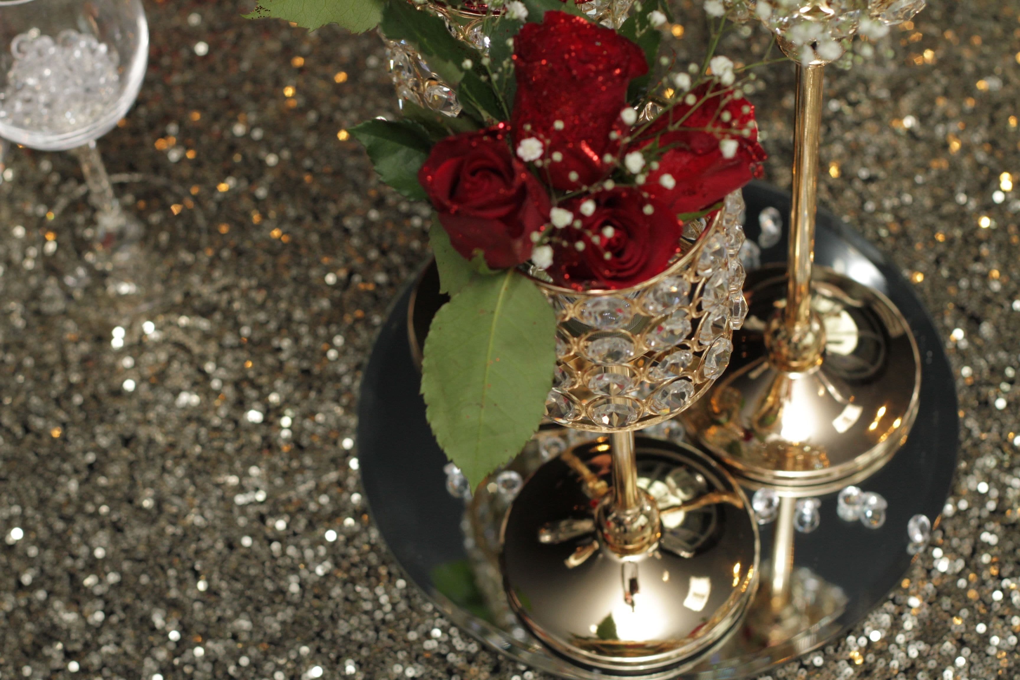 A decorative glass vase with red roses and white flowers on a reflective surface.