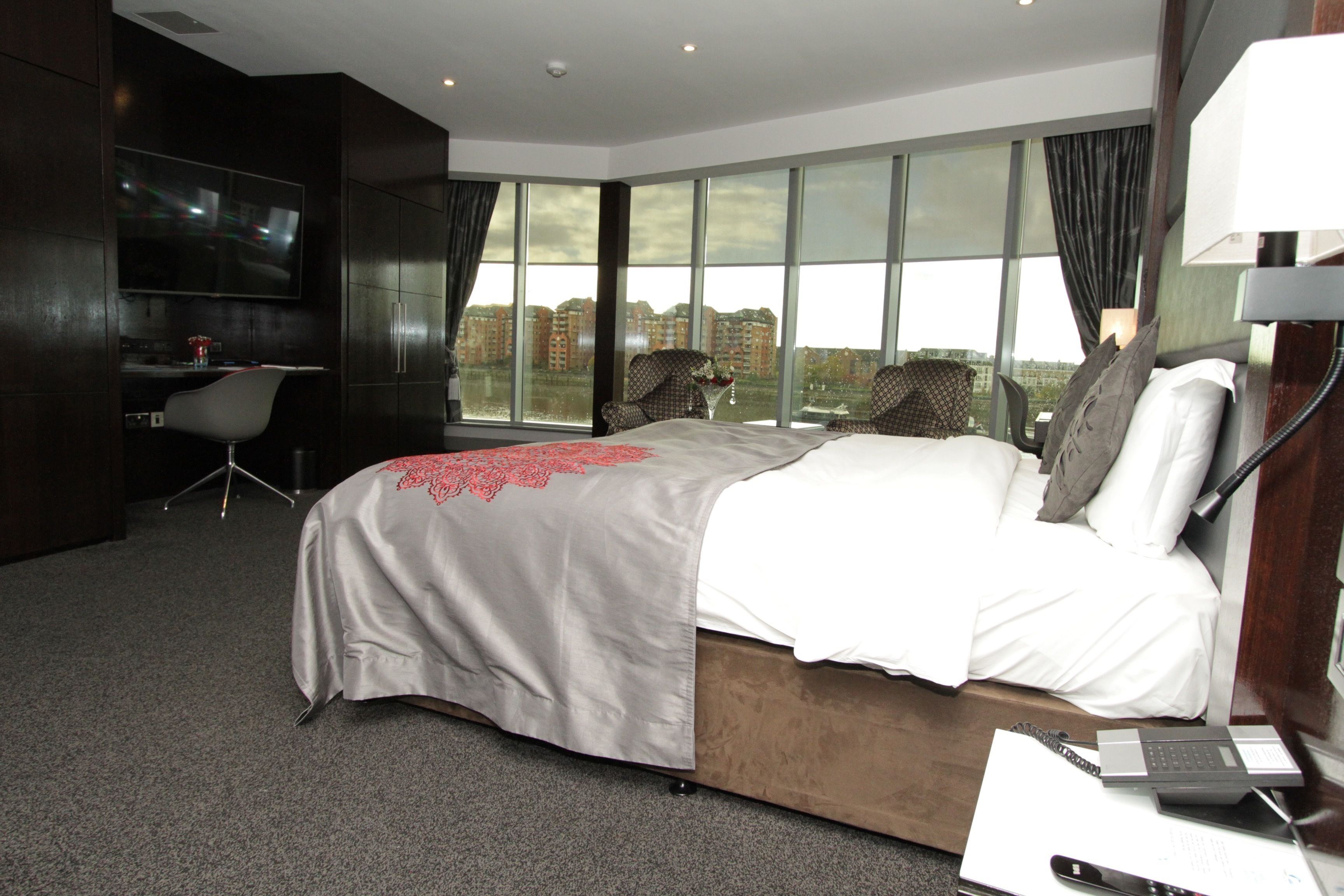 Ein modernes Hotelzimmer mit einem großen Bett, einem Schreibtisch mit Computer, einem Fernseher und Blick auf die Stadt.