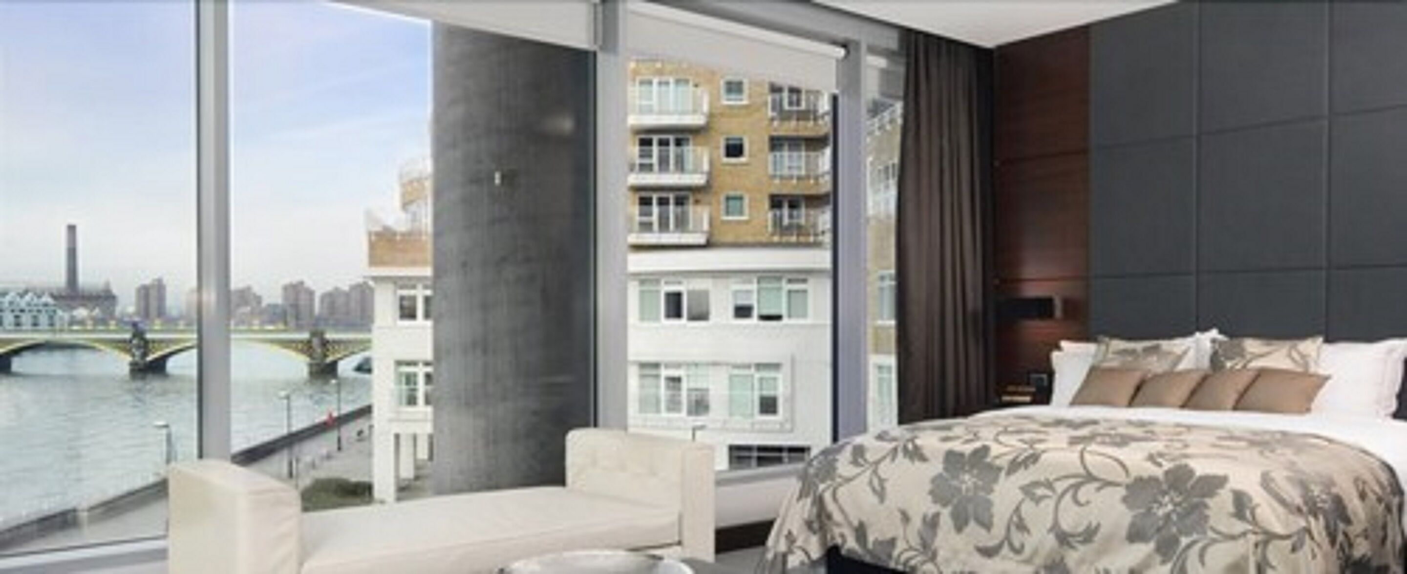 A modern hotel room with a large bed, a sofa, and a view of a river and buildings.