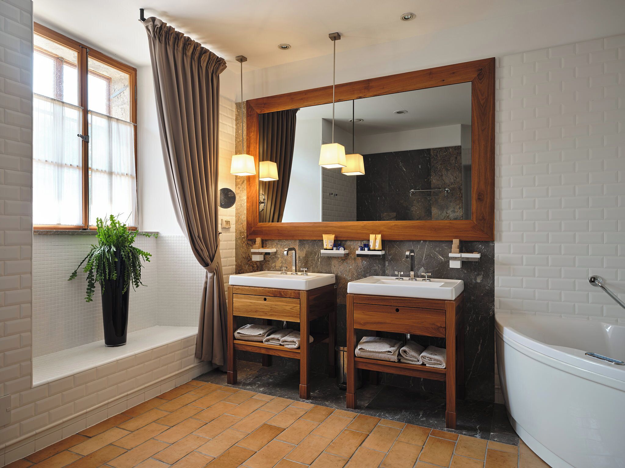 A modern bathroom with two sinks, a large mirror, and a potted plant.