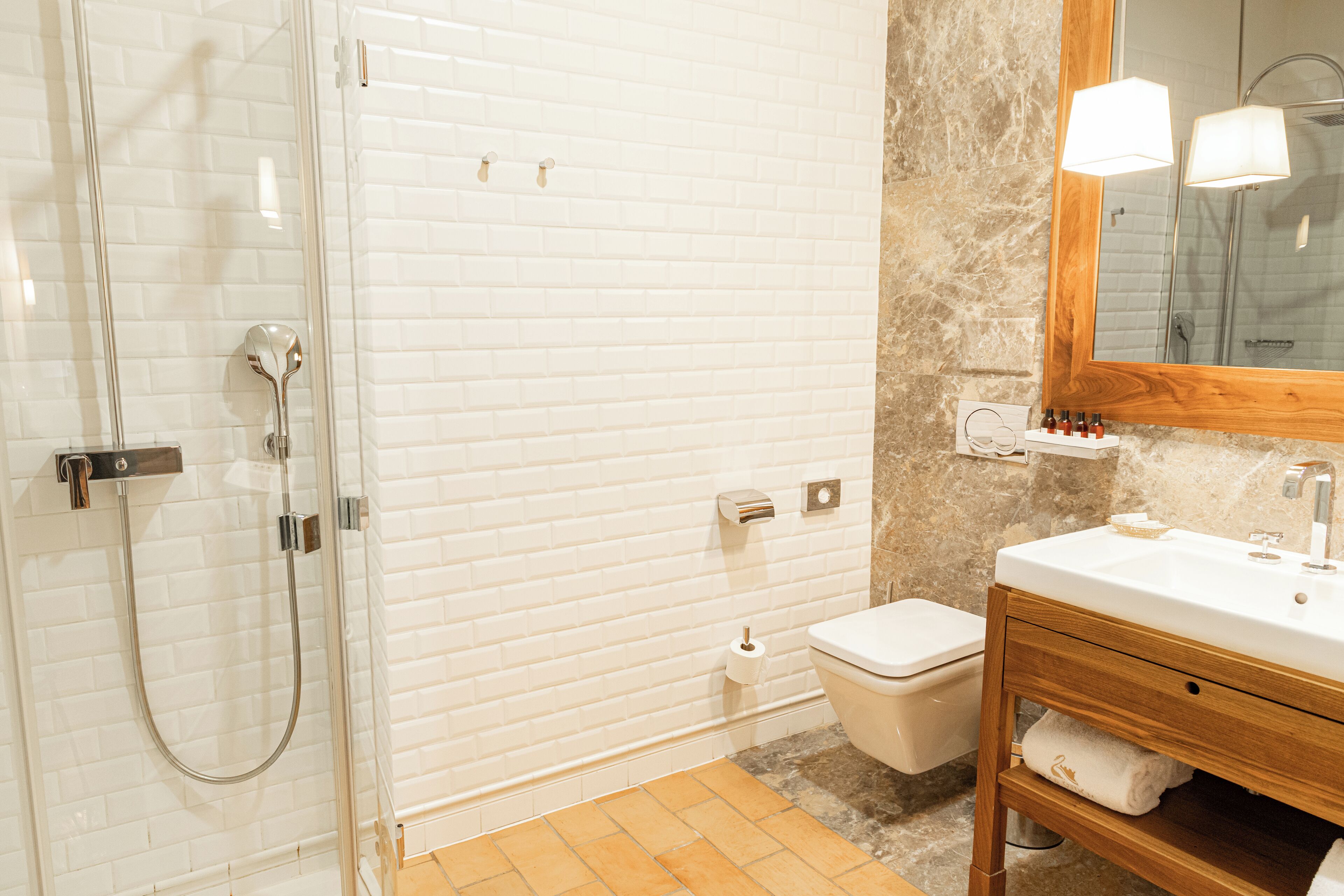 Un baño con ducha envuelta en vidrio, inodoro blanco y tocador de madera con espejo.