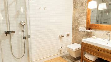 Un baño con ducha envuelta en vidrio, inodoro blanco y tocador de madera con espejo.