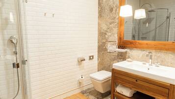 A bathroom with a glass shower enclosure, a white toilet, a wooden vanity with a mirror, and a marble backsplash.