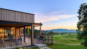 A modern building with a wooden exterior and a covered outdoor seating area with tables and chairs. - Hotel Grad Otocec Relais & Châteaux (Novo Mesto)