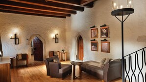 A cozy interior with wooden flooring, a sofa, a chair, and a table. There are wall sconces and framed pictures. - Hotel Grad Otocec Relais & Châteaux (Novo Mesto)