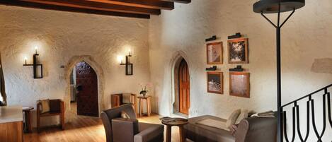 A cozy interior with wooden flooring, a sofa, a chair, and a table. There are wall sconces and framed pictures.