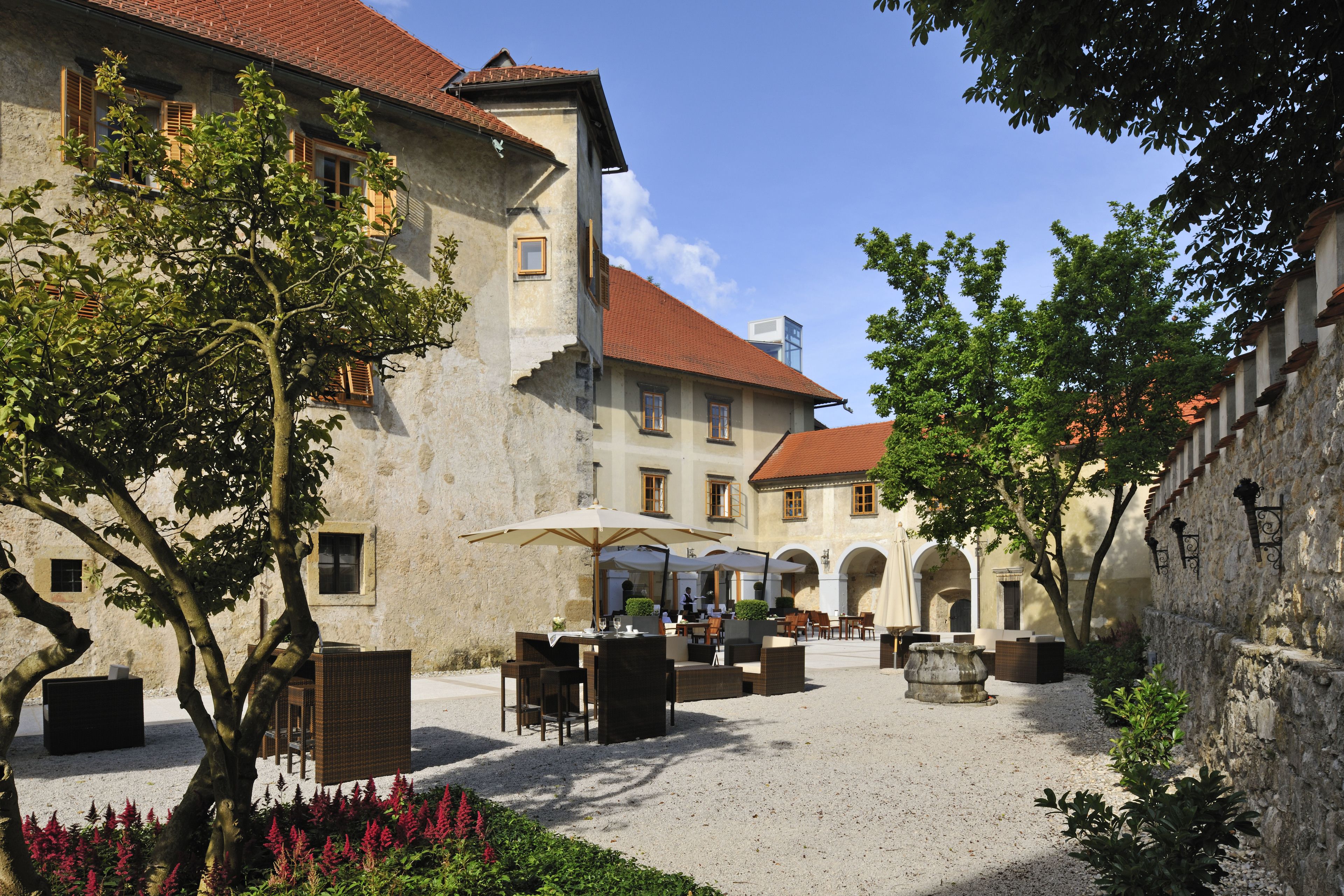 A courtyard with outdoor seating, a building with a red-tiled roof, and stone walls.