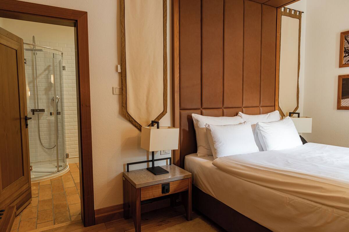 Ein Hotelzimmer mit einem Bett, Nachttischen, einem Spiegel und einer Duschkabine.