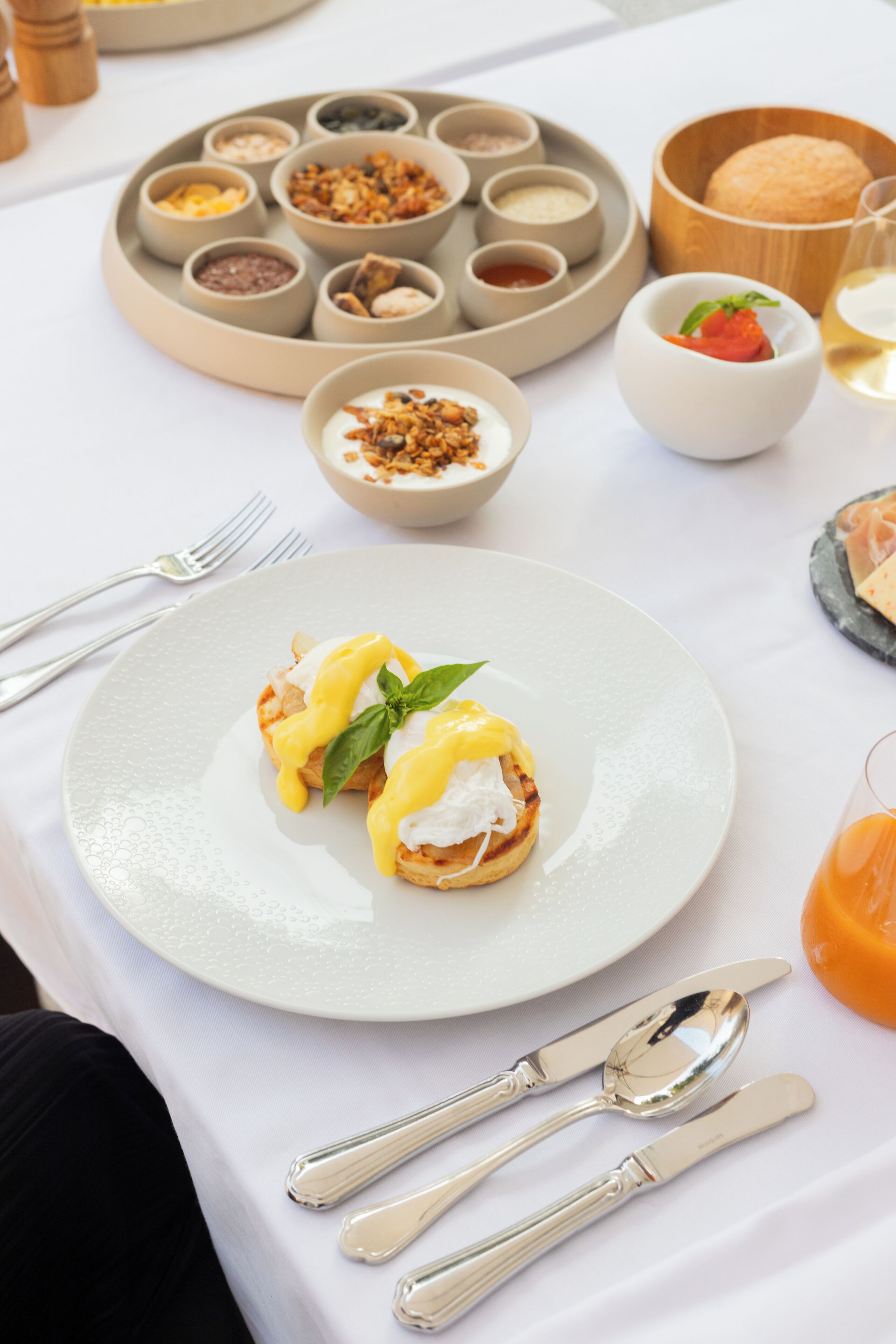 A breakfast setting with a plate of eggs benedict, a variety of condiments, and a glass of orange juice.