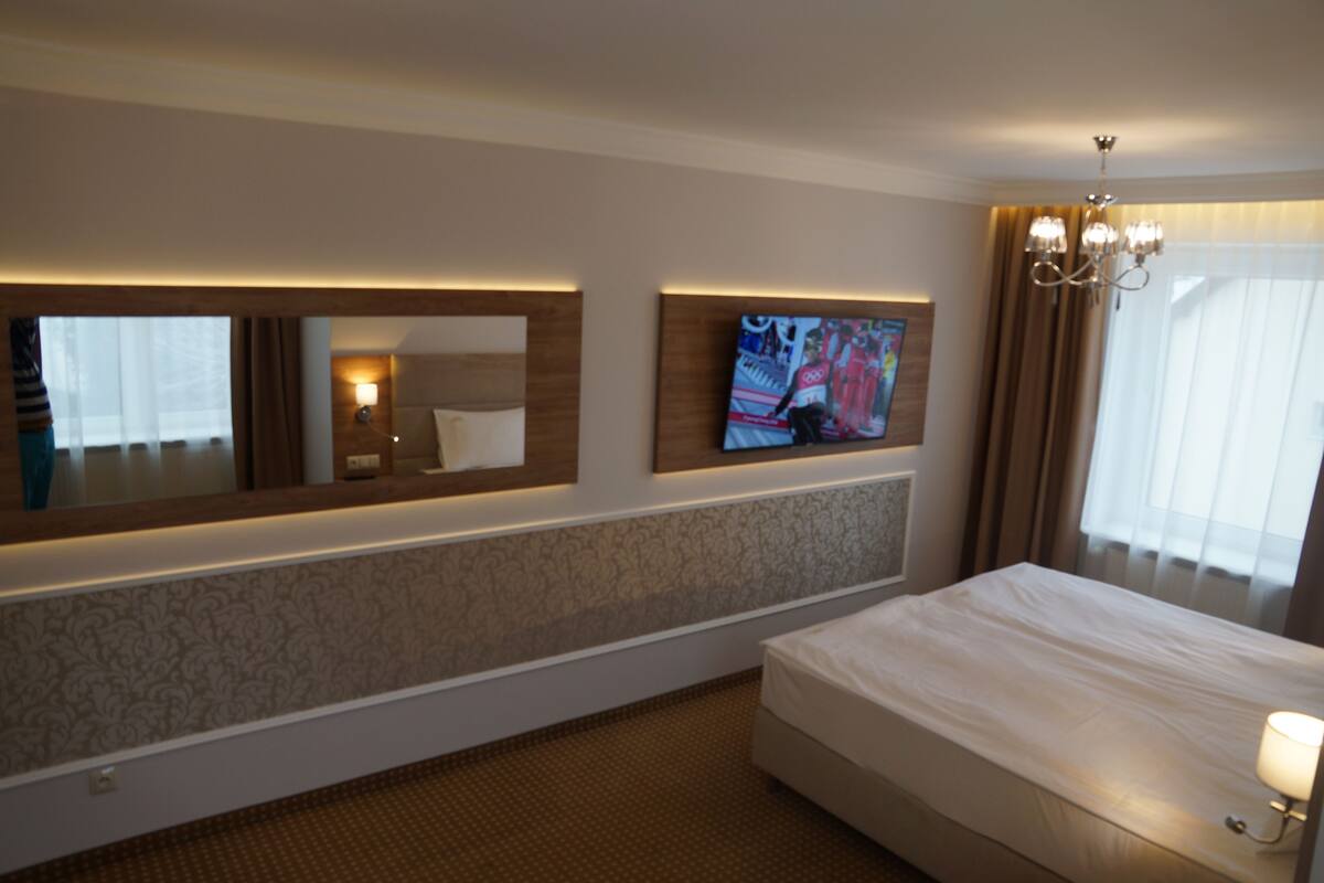 Quarto de hotel com uma cama grande, televisão fixada na parede e espelho sobre a cama.