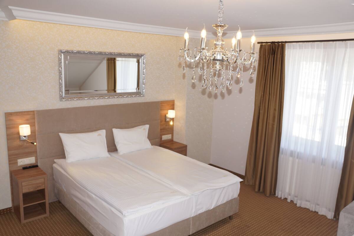 Quarto de hotel com uma cama grande, um candelabro, um espelho e cortinas.