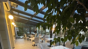 An outdoor seating area with tables and chairs, surrounded by glass walls and potted plants. - Moris Boutique Beach Hotel (Gdansk)